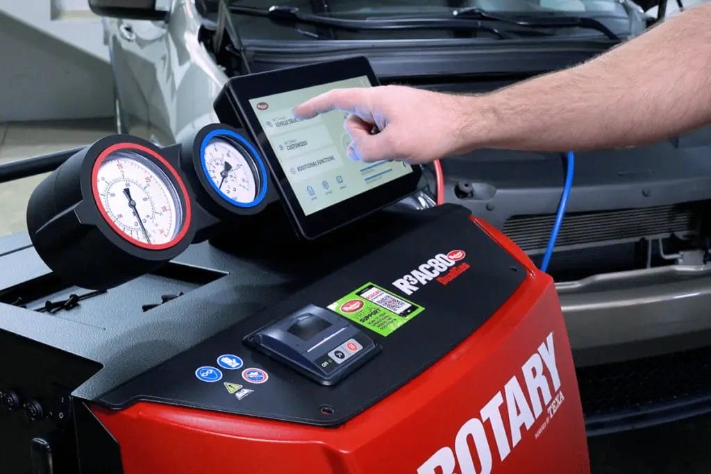 Rotary AC service cart with digital interface and pressure gauges in an automotive repair shop.